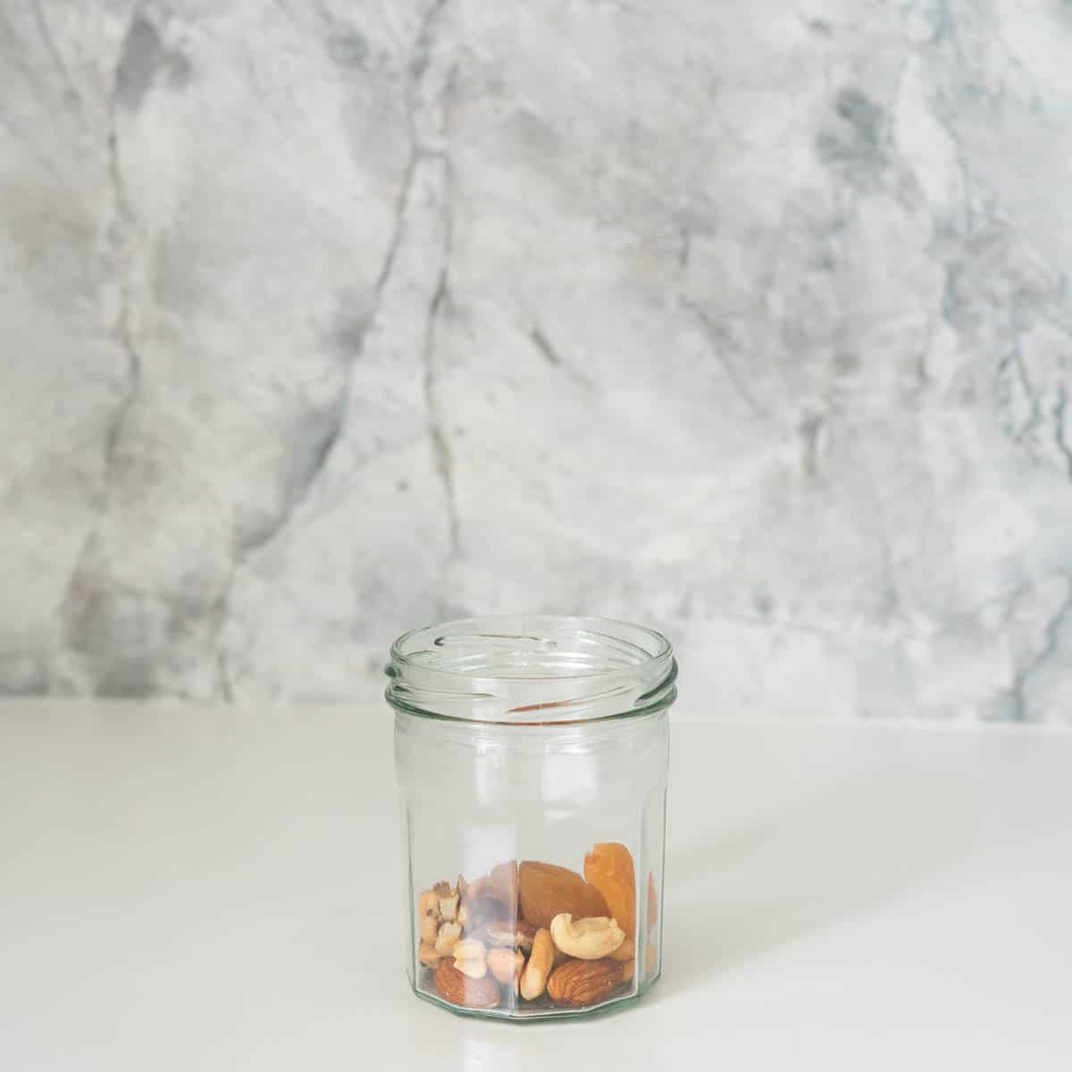 A small jar, one quarter filled with nuts and dried apricots.