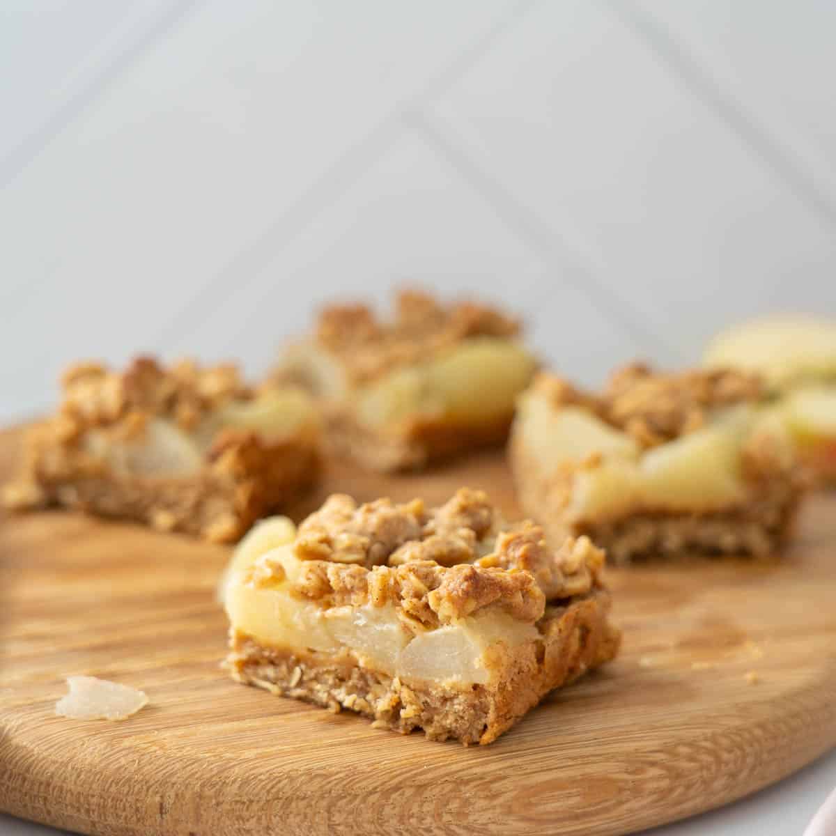 A piece of apple oat slice sitting on a round wooden board.
