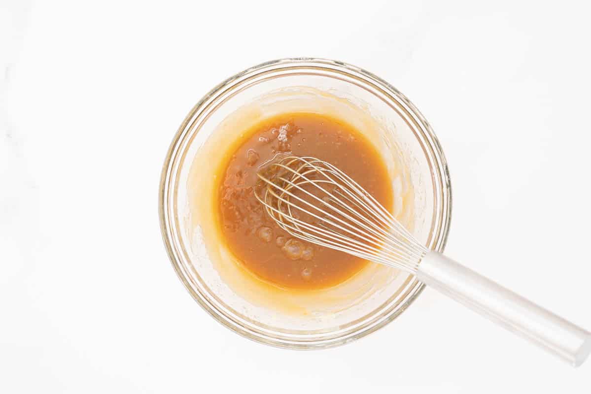 A caramel coloured mixture in a large mixing bowl with a whisk.