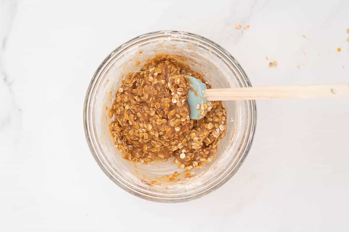 A large glass mixing bowl containing an oat based slice mixture.