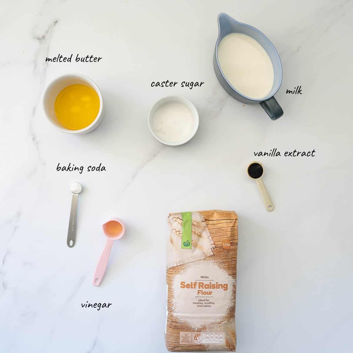 The ingredients to make pancakes without eggs laid out on a bench top with text overlay.