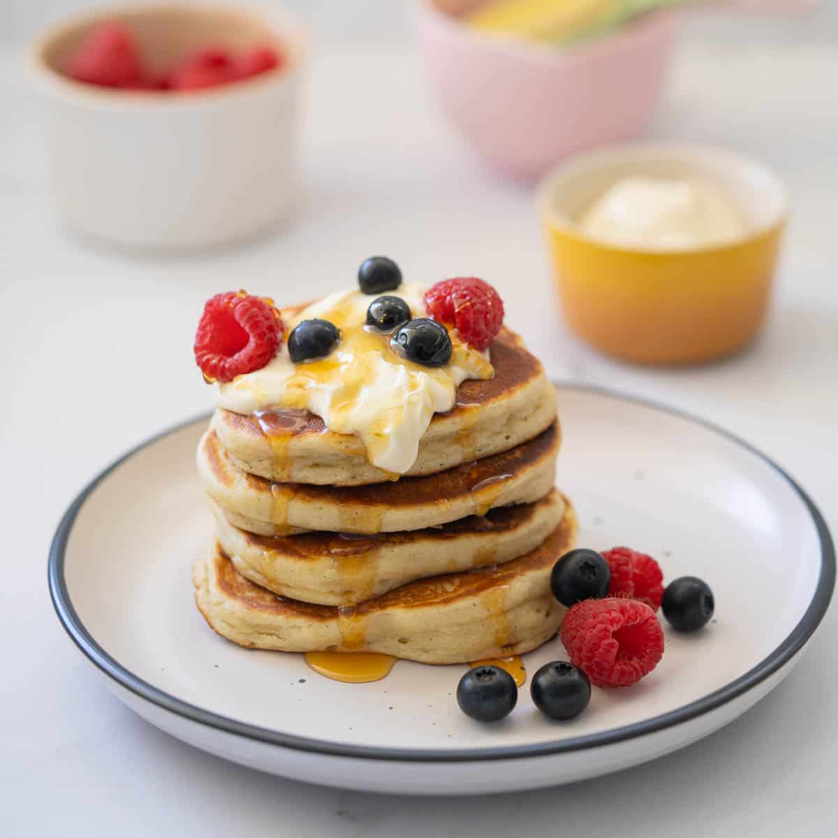 Four thick pancakes stacked on a tower topped with yoghurt, berries and yoghurt. 