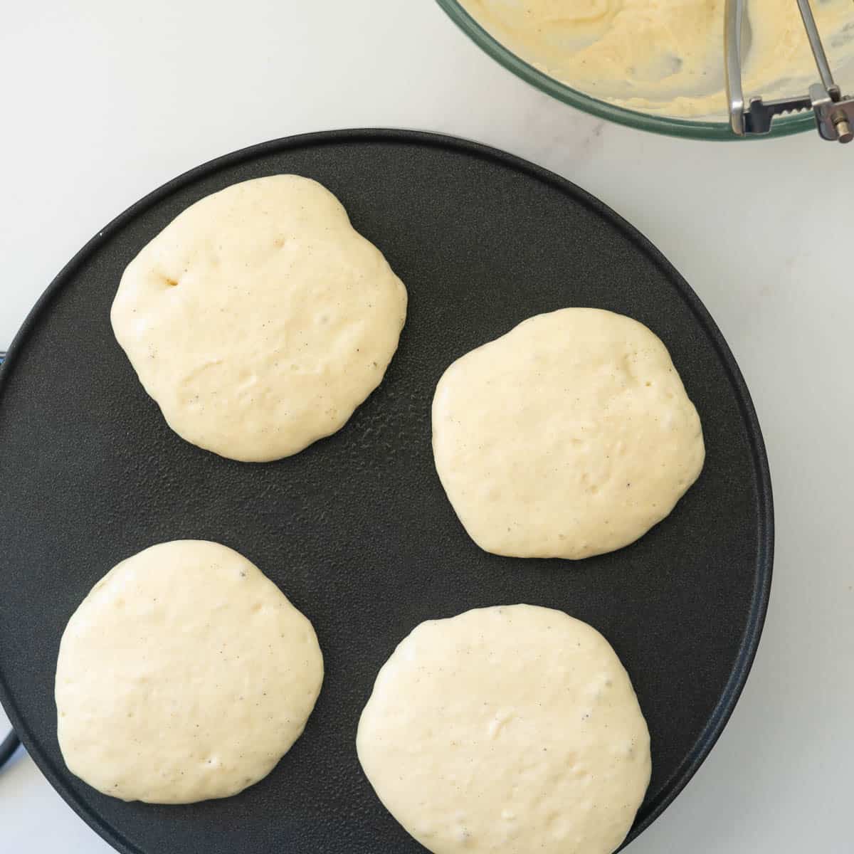 Four pancakes on a hot plate cooking.
