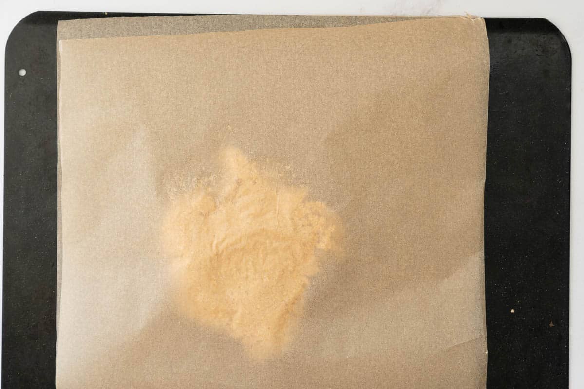 A ball of cracker dough sandwiched between two pieces of baking paper on a baking tray.