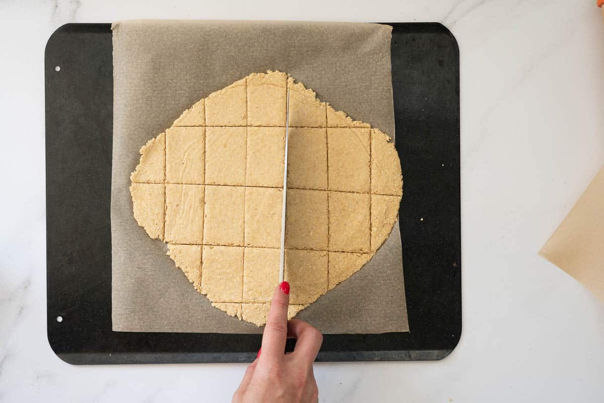 Cracker dough beeing scored into rectangular shapes with a knife.