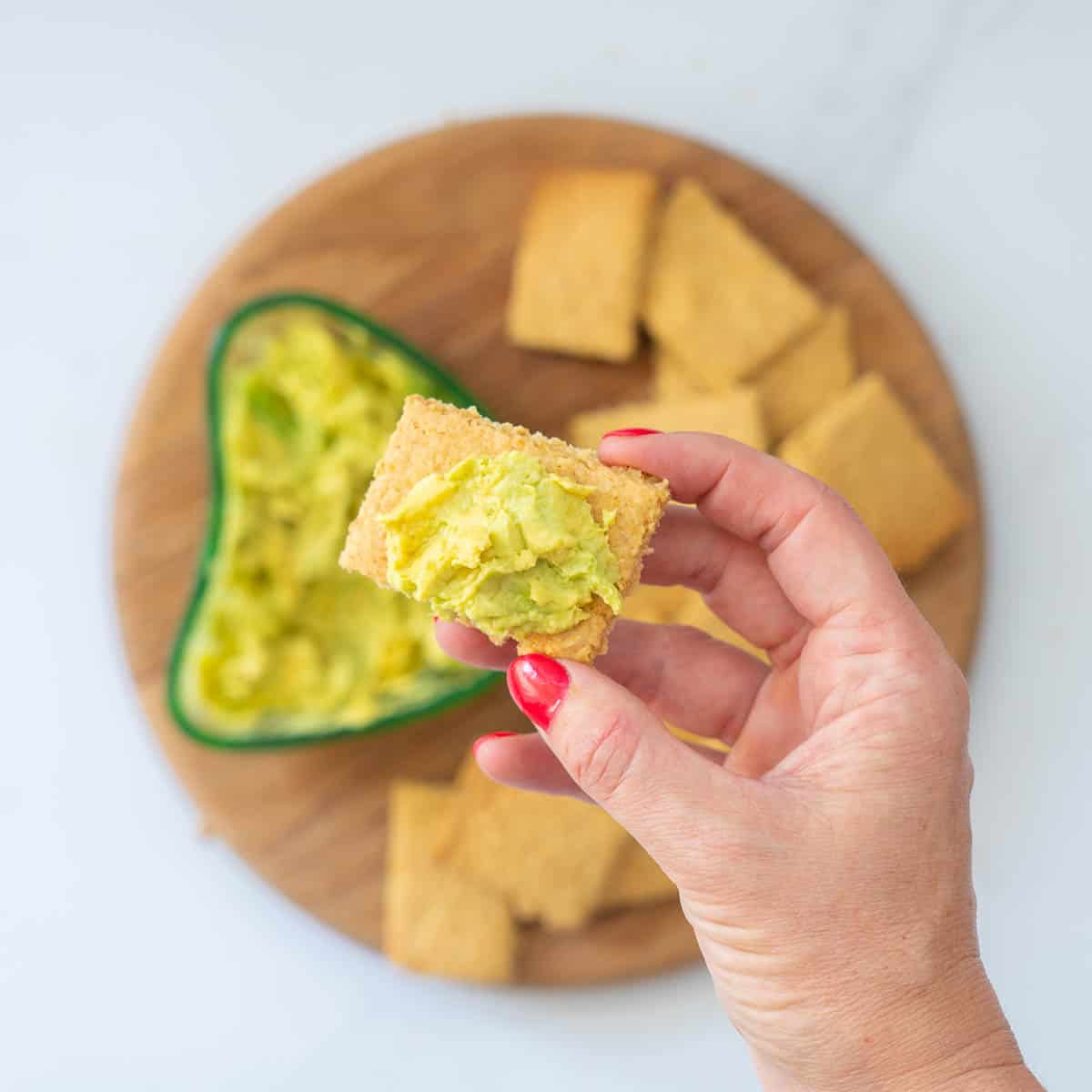 An oat cracker topped with avocado being held up to the camera.