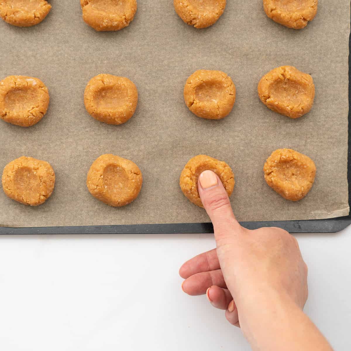 A thumb being pressed into a ball of cookie dough to create a depression.