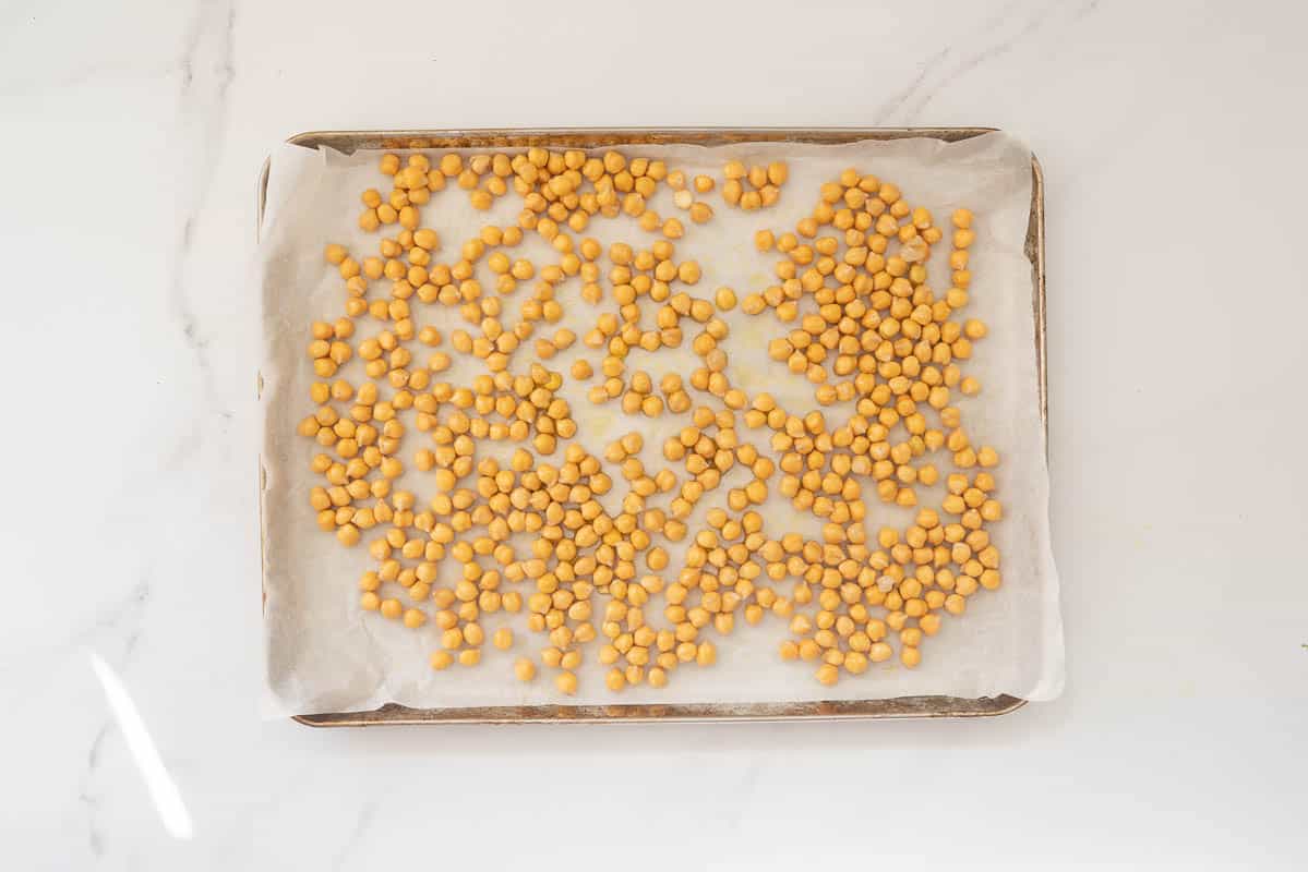 Oiled chickpeas on a baking lined roasting tray.