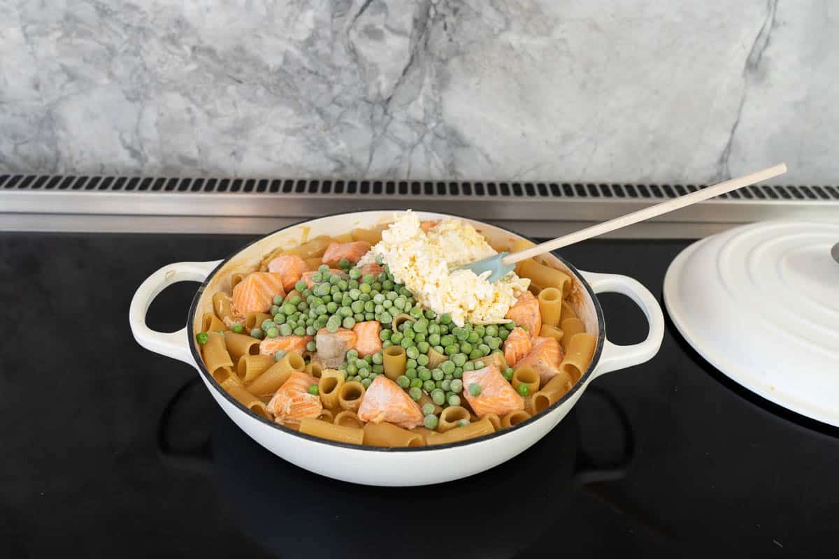 A mix of cheese and sour cream and frozern peas being stirred through cooked pasta.