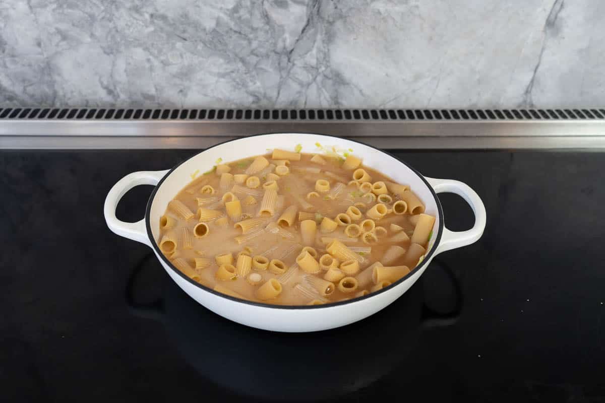 Pasta sitting in liquid in a large casserole dish on a stove top.