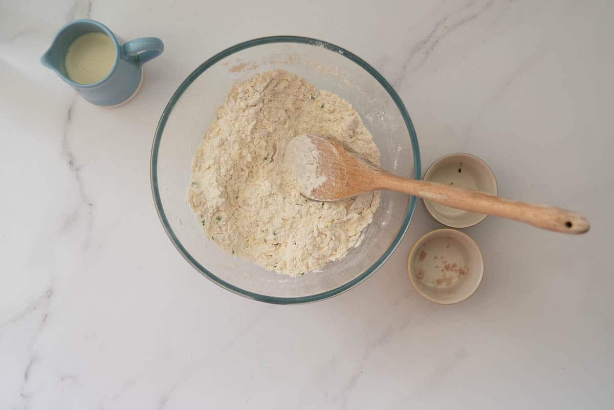 Cheese, ham, chives mixed through flour in a large glass mixing bowl.