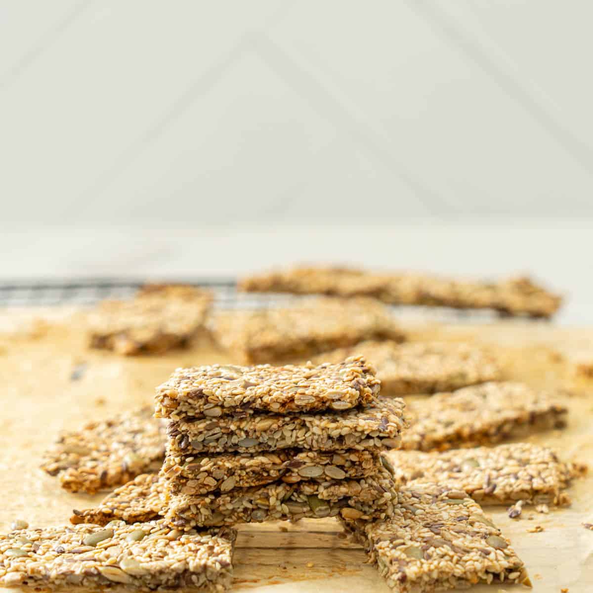 A stack of four very seedy crackers on a baking paper lined cooling rack.