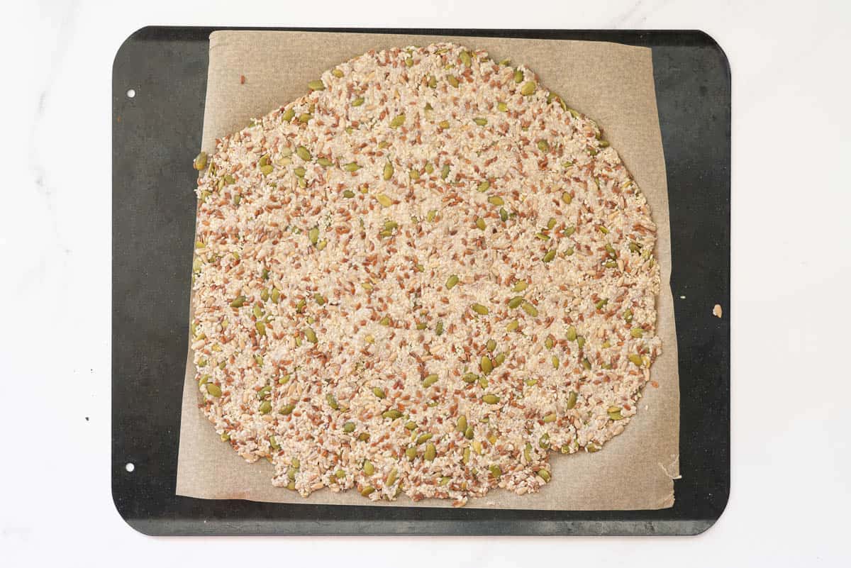 Seeded crackers mix, flattened on a baking paper lined tray ready to be baked.