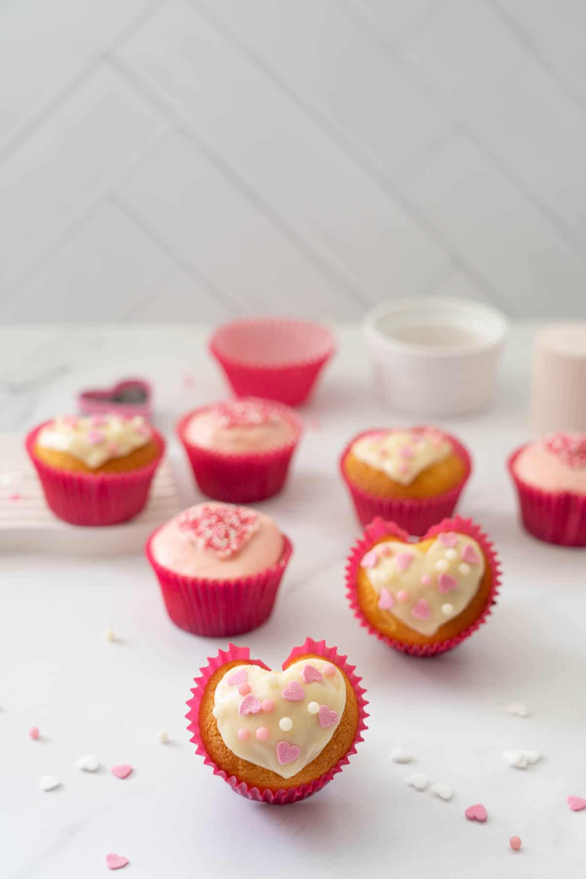 A heart shaped cupcake, decorated with pink and white on a white marble bench.