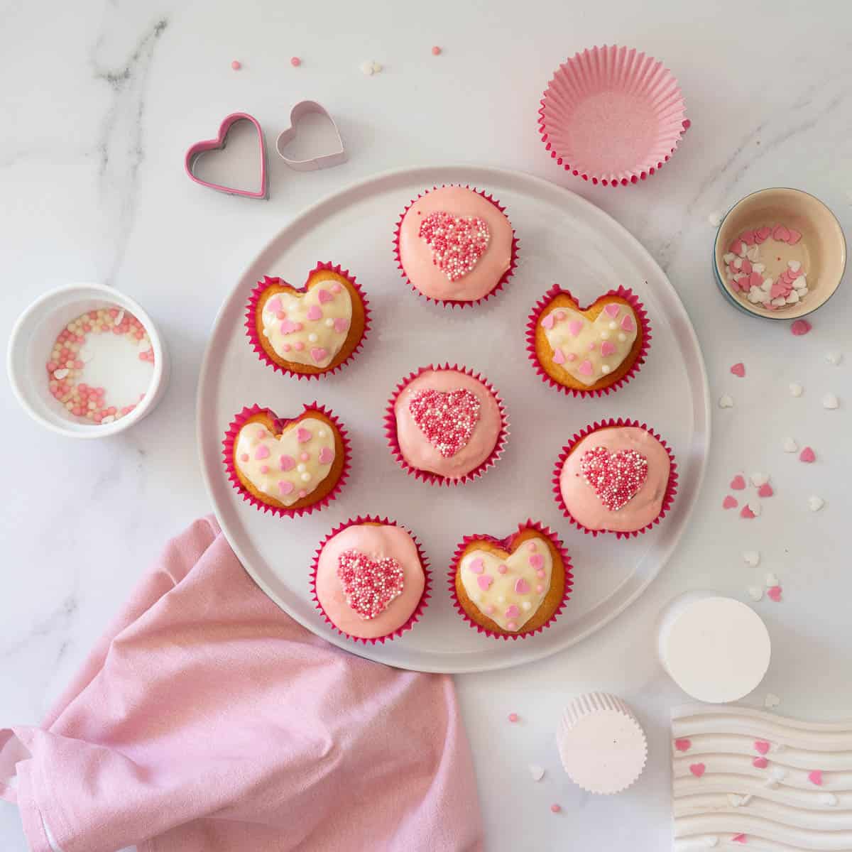 Cupcakes decorated with white and pink icing and sprinkles on a white plate.