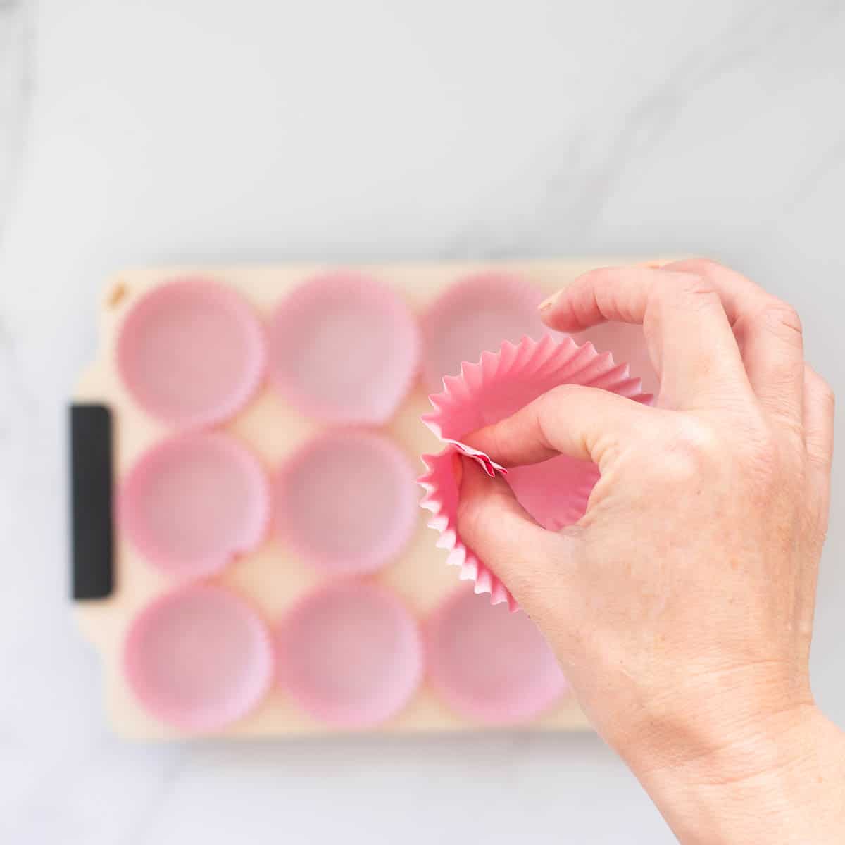 A pink cupcake case being pinched together to create a fold using the fore finger and thumb.