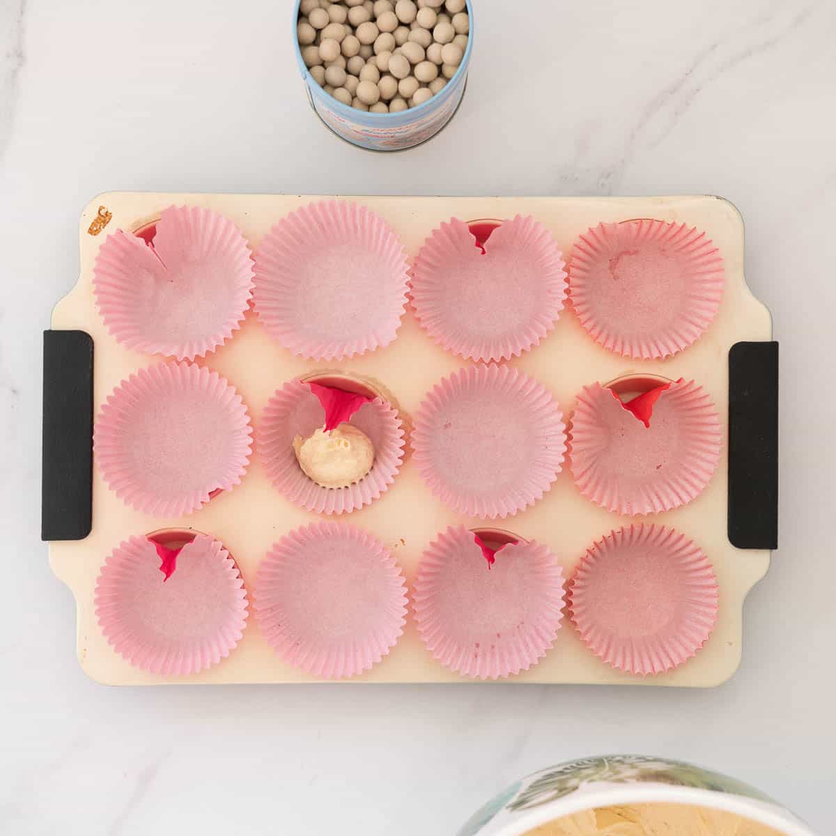 A cupcake liner with a fold in it, sitting in a cupcake tray, partially filled with cupcake batter.