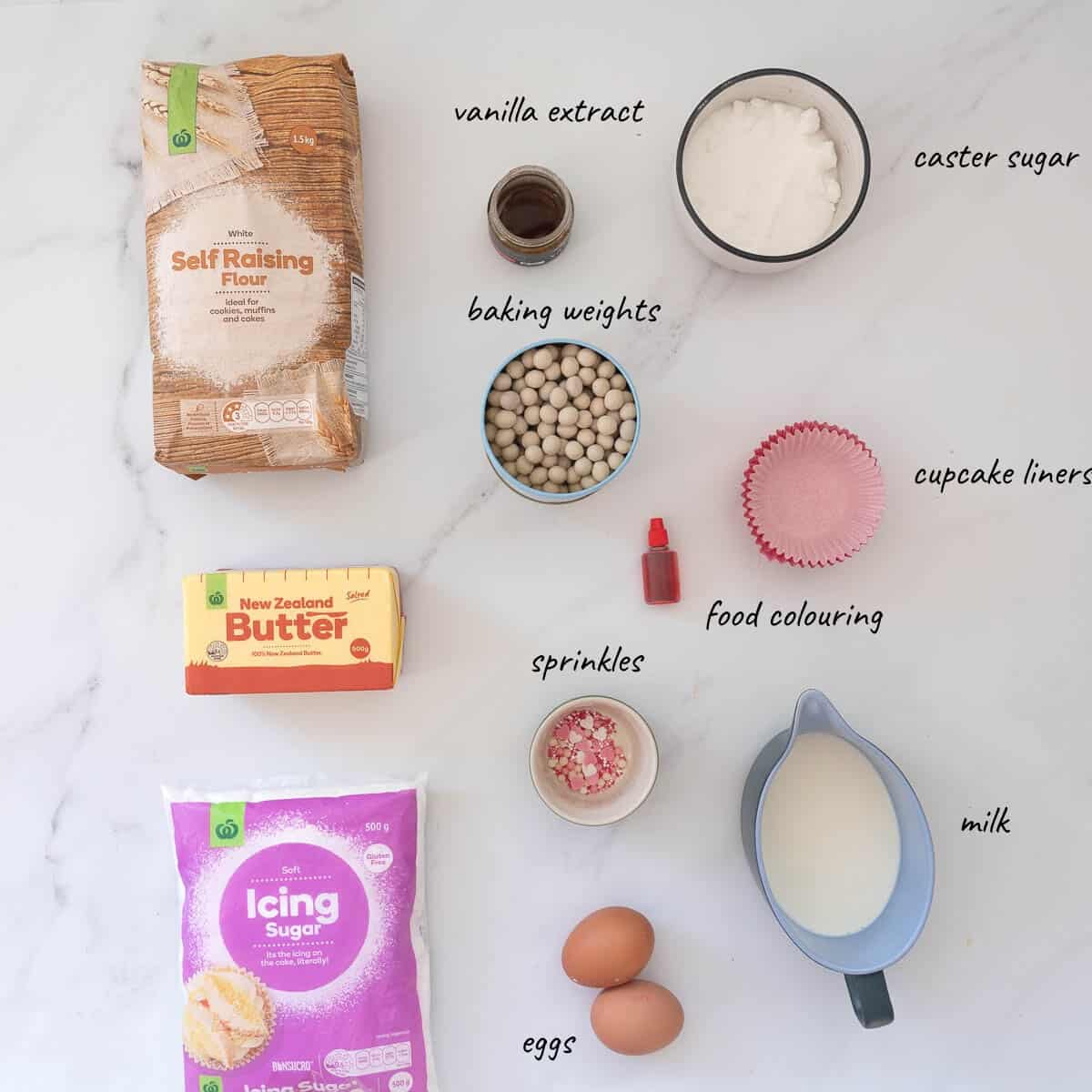 The ingredients to make valentines cupcakes laid out on a bench top with text overlay.