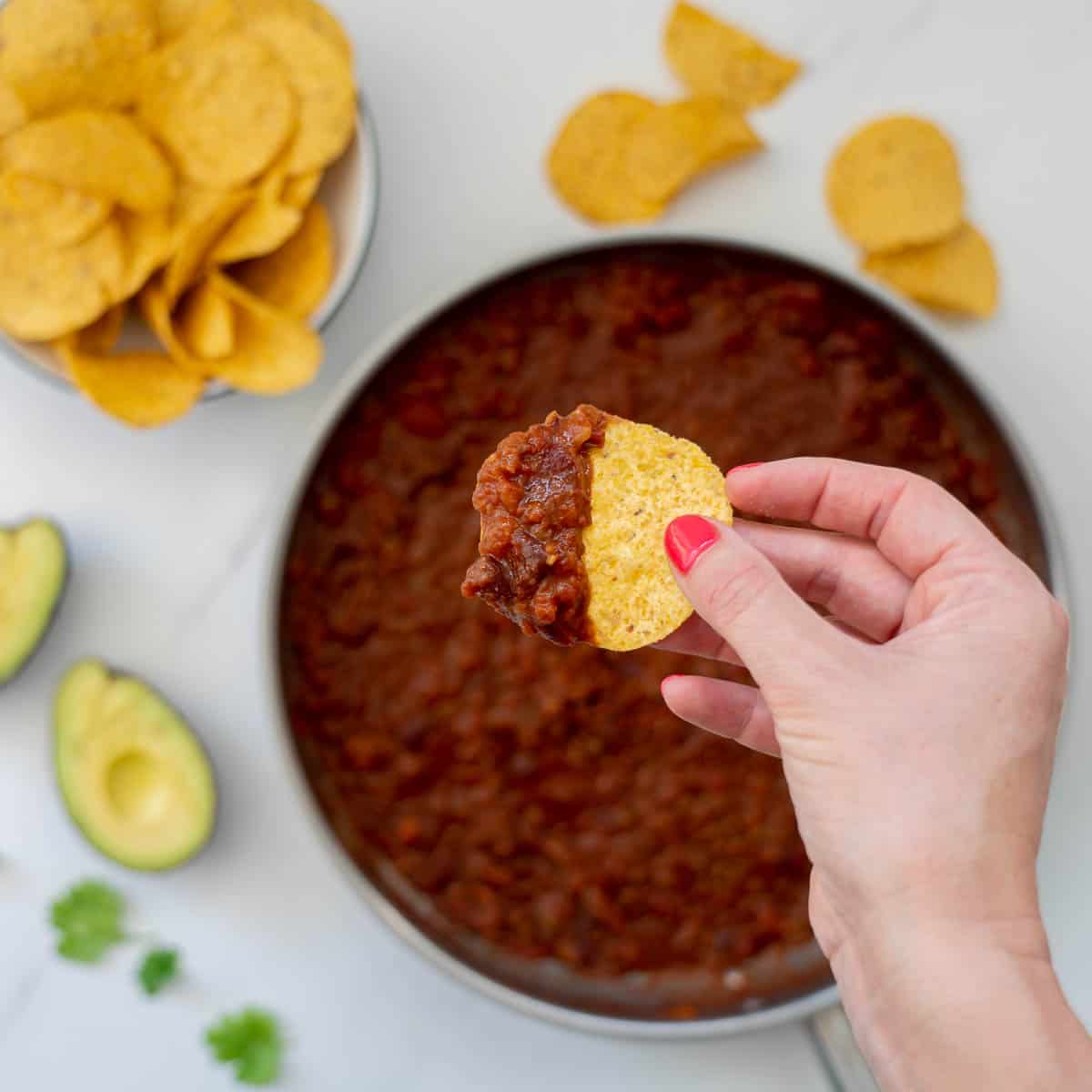 A corn chip loaded with bean based nacho mix being held above a dinner table.