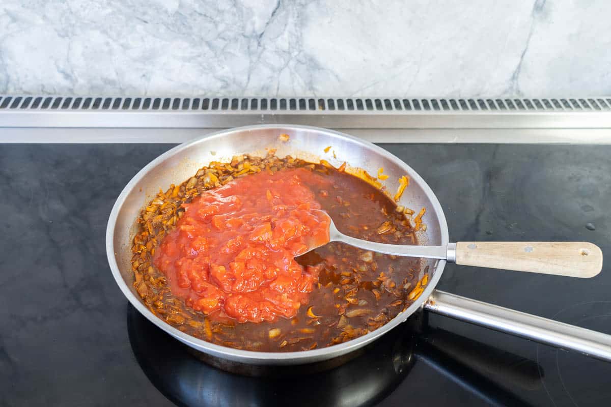 Tinned tomatoes being added to a fry pan.