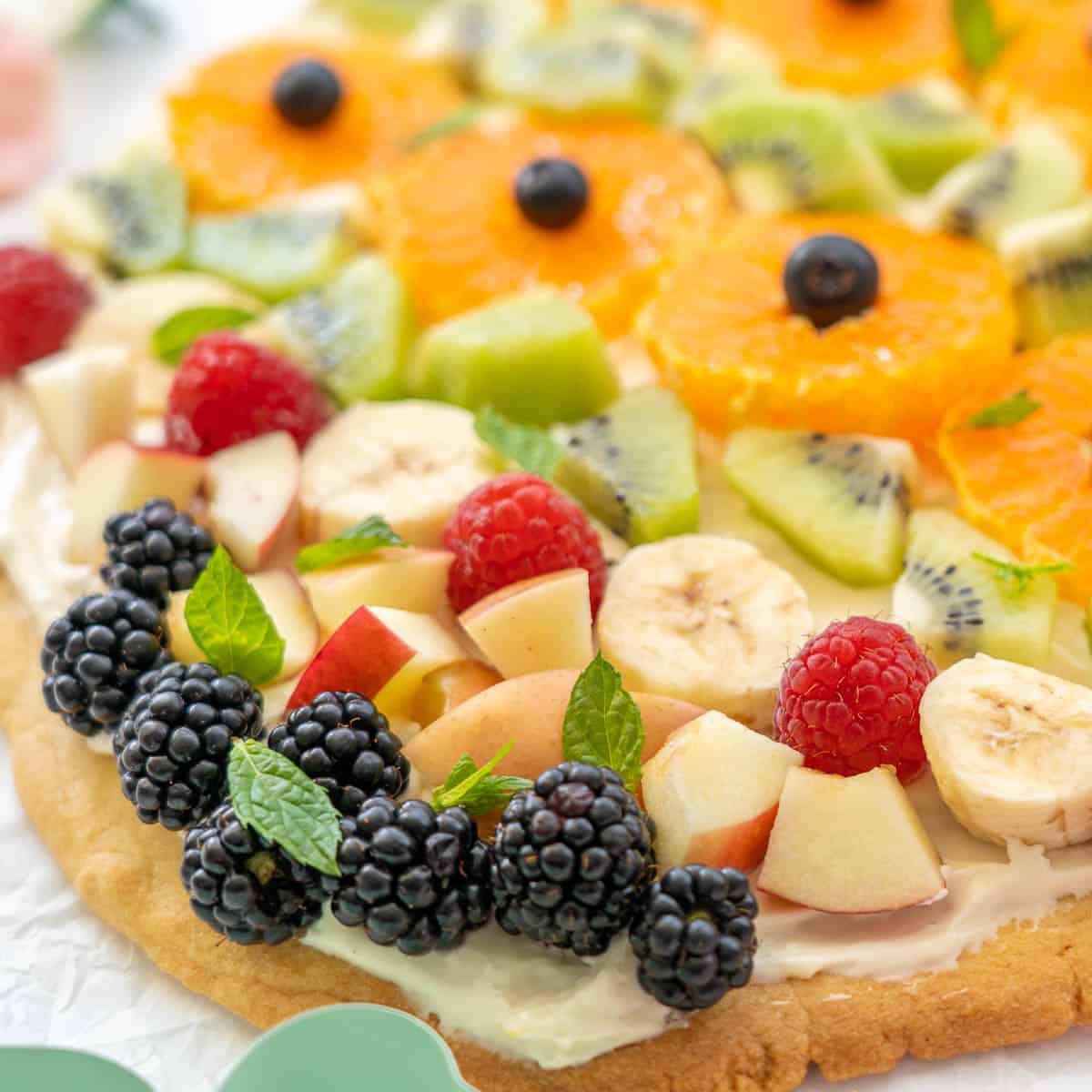 Fresh fruit covering a large sugar cookie pizza base, blackberries, pieces of apple, kiwi