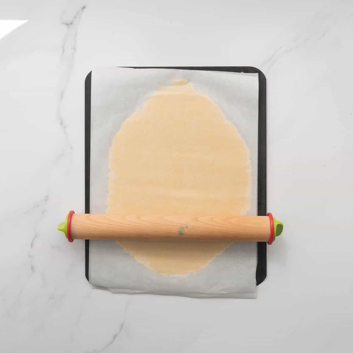 Cookie dough being rolled out while sandwiched between 2 pieces of baking paper