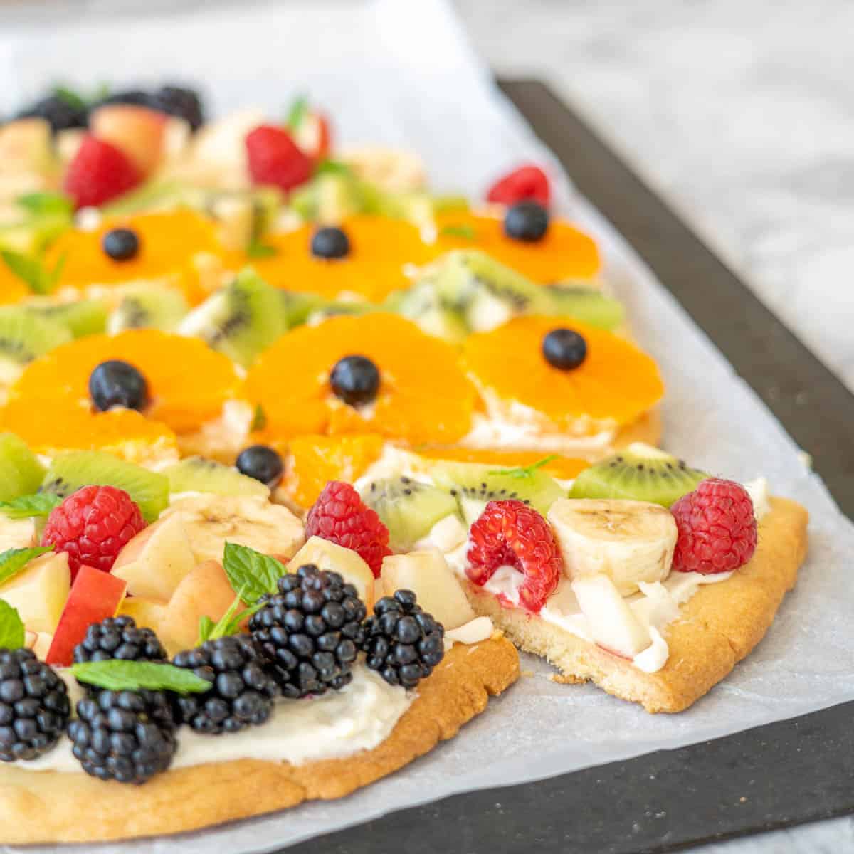 A slice of fruit pizza being removed from a full fruit pizza.