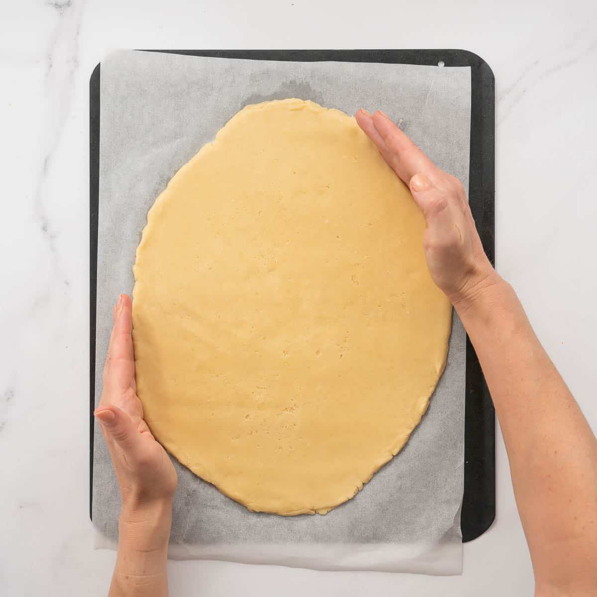 A cookie dough pizza base being shaped into an egg shape by two hands.