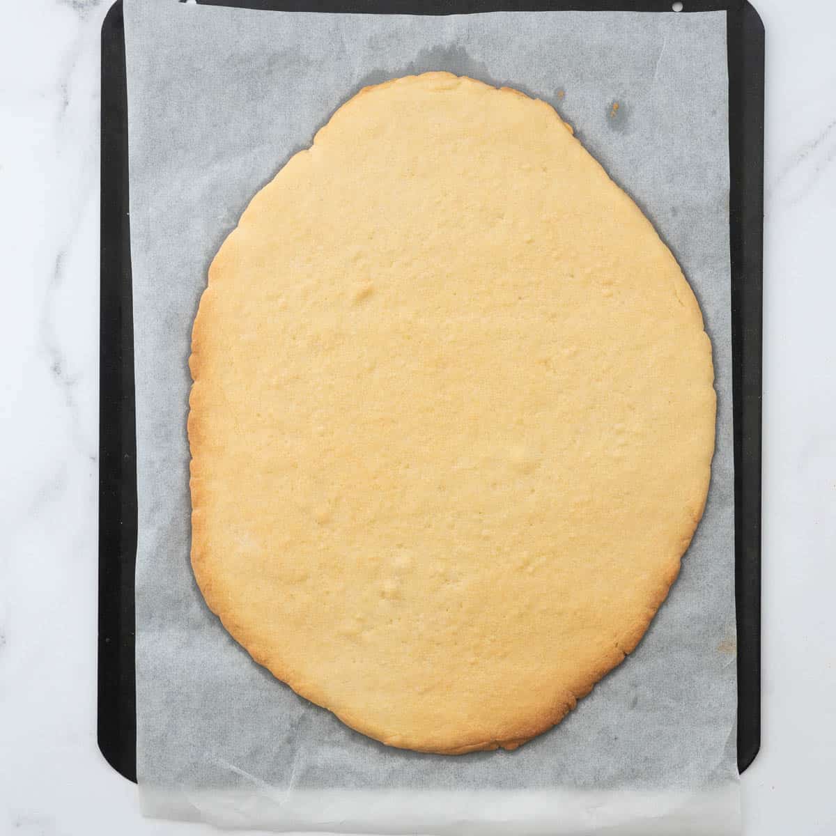 A large pizza based sized sugar cookie baked into an egg shape, the cookie is golden brown around the edges.