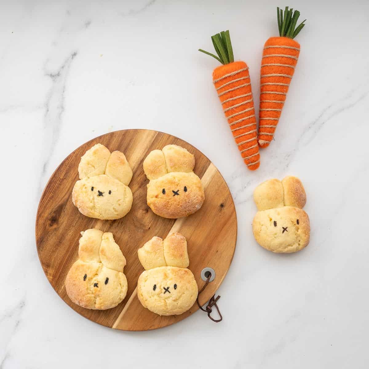 Four dinner rolls in the shape of bunnies on a round wooden board.