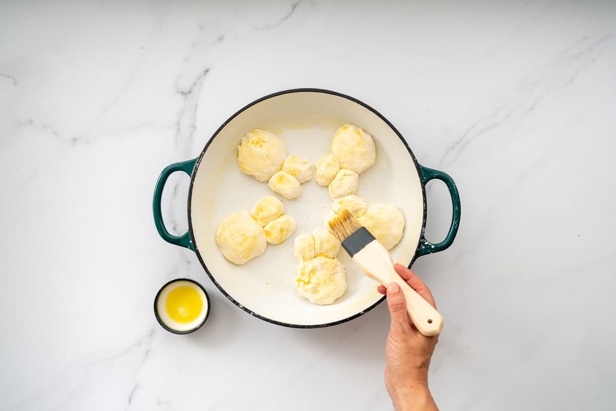 Five bunny buns in a white enamel dish being brushed with melted butter.