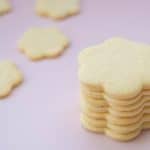 A tower of flower shaped cookies on a pink background.