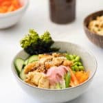 A bowl of teriyaki chicken Rice, vegetables and toasted seaweed pickled ginger and sesame seeds.