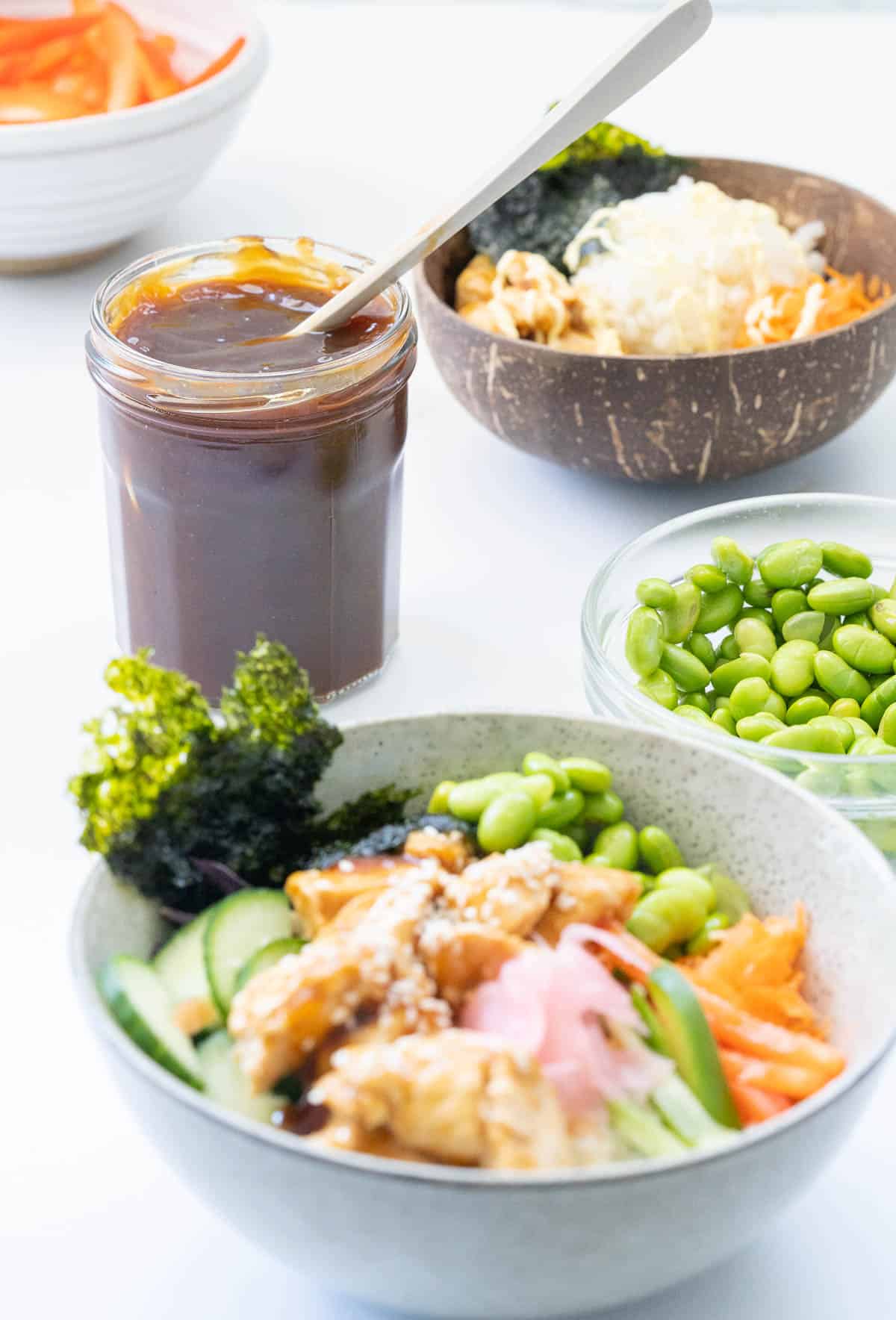A bowl of teriyaki chicken vegetables and rice in a bowl with a jar of teriyaki sauce in the background.