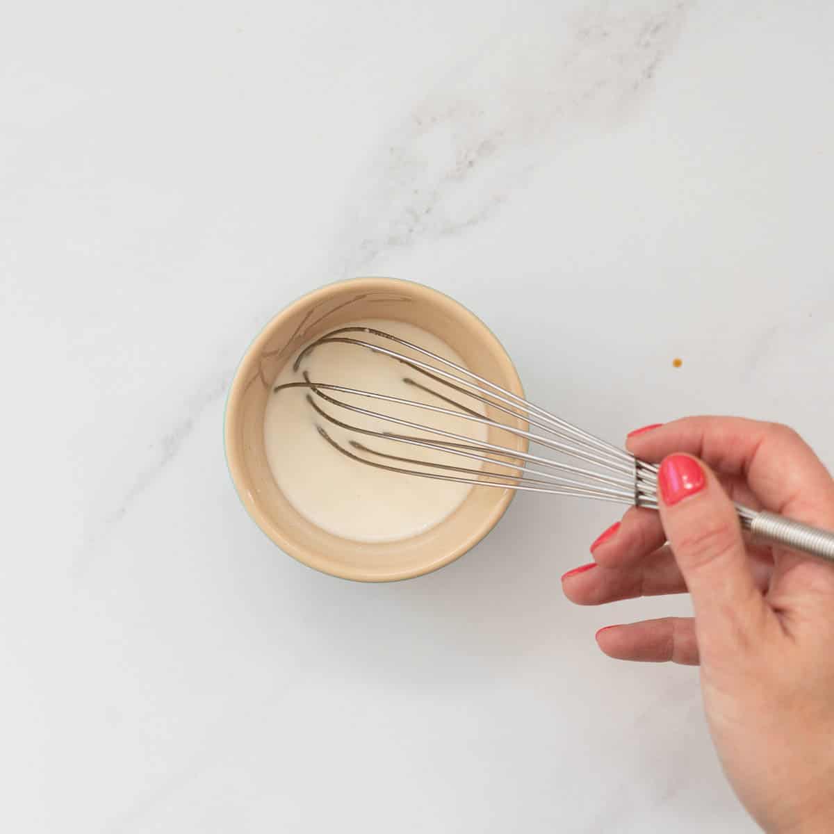 A hand whisking together corn flour and water to create a slurry.