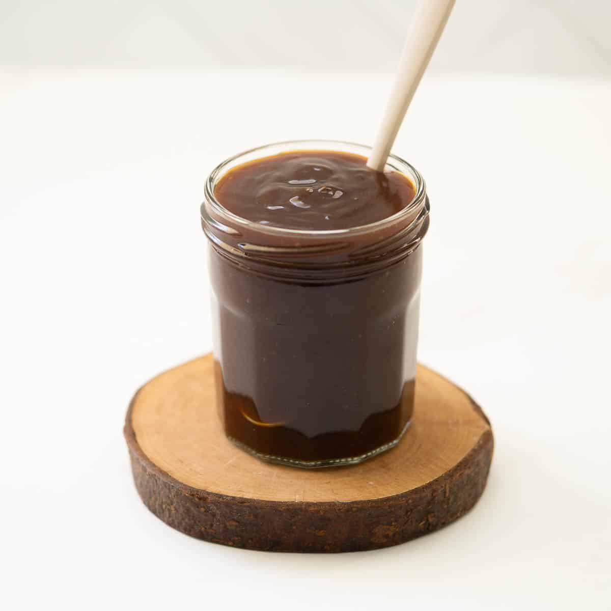 A glass jar full of teriyaki sauce sitting on a wooden coaster,