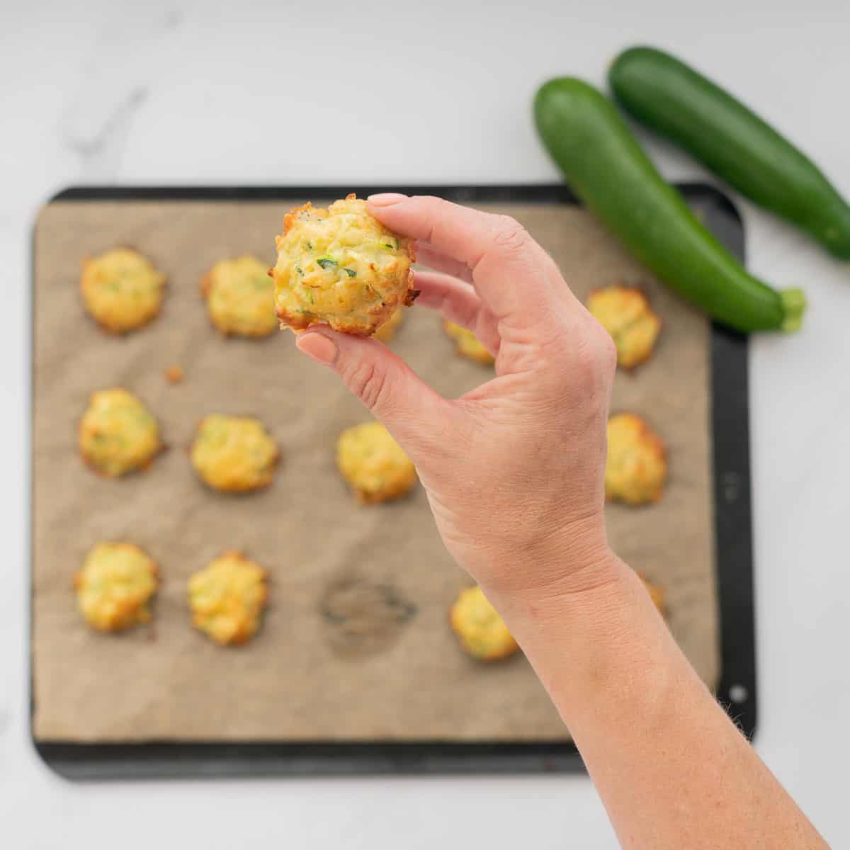 A zucchini bite being held above a tray of zucchini tots.