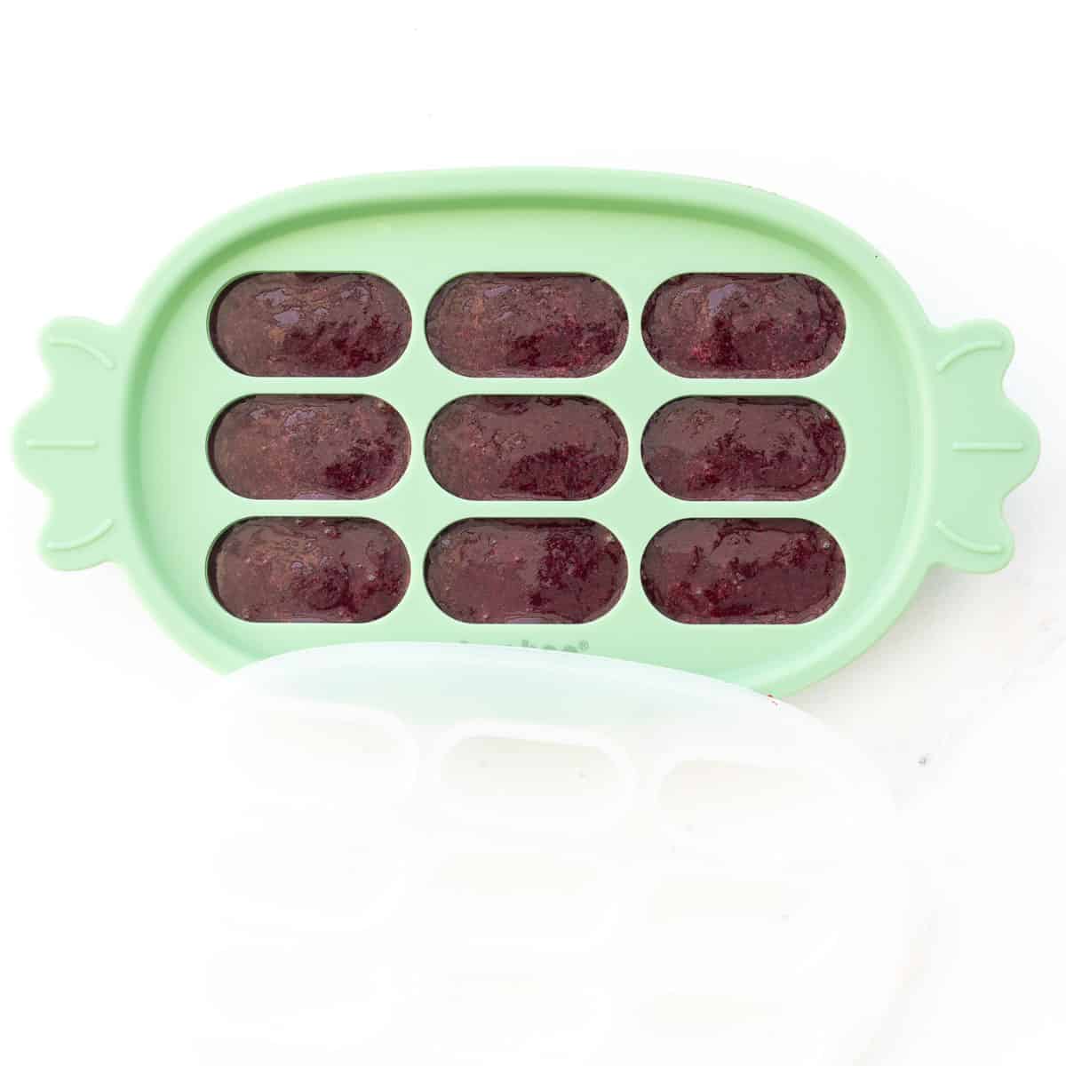 Purple baby food in a green silicone ice cube tray.
