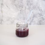 Purple blueberry puree in a small glass jar with a blue bamboo spoon in front of a marble splash back.