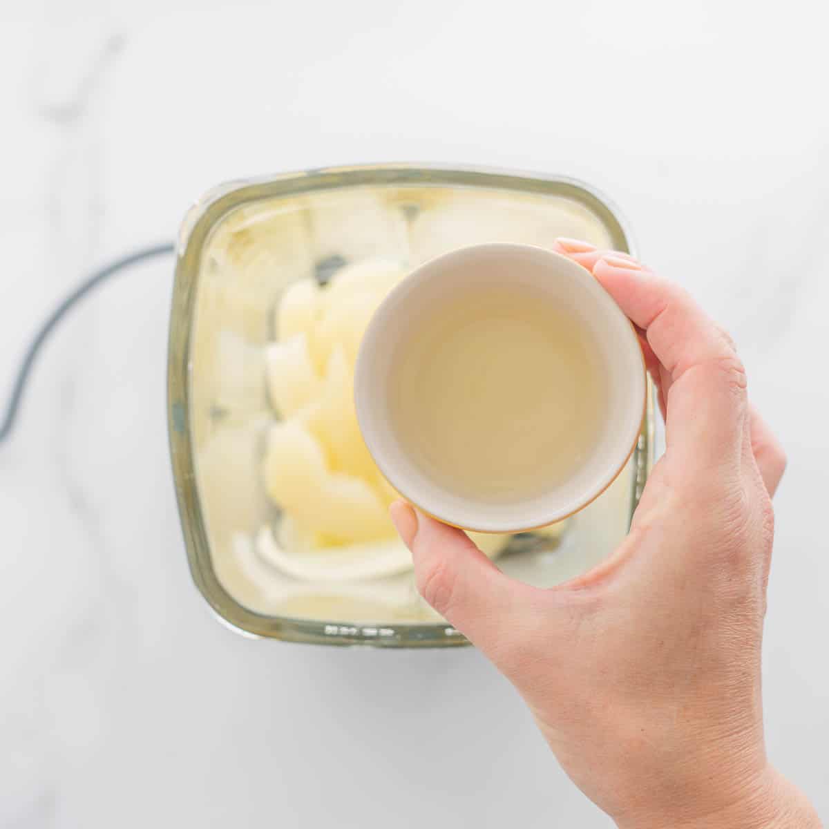 A small bowl of pear liquid held above a blender jug of sliced pears.