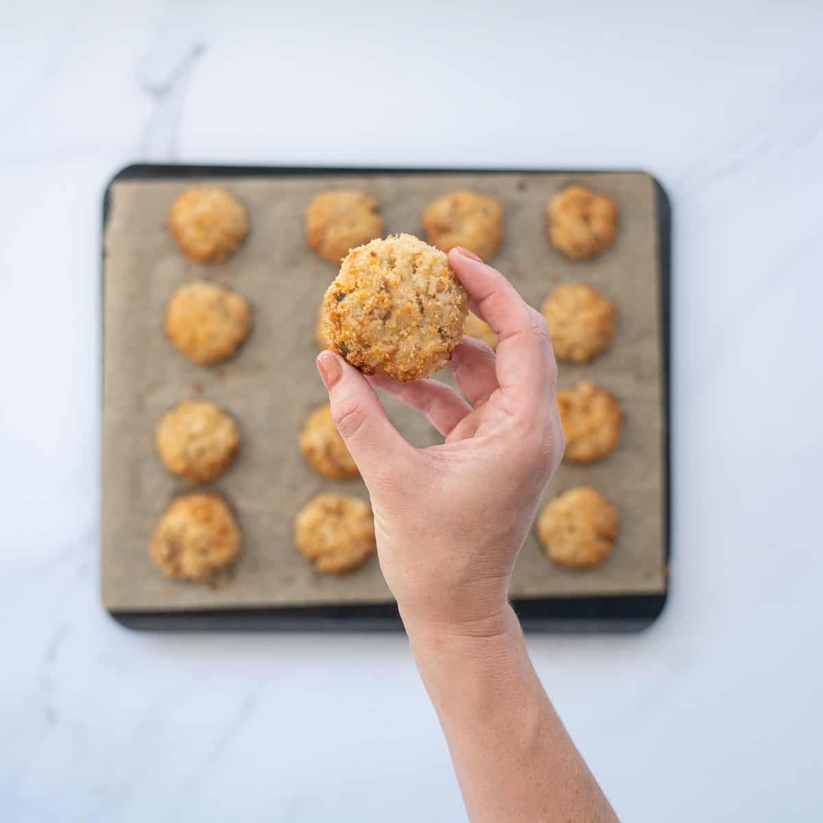 A golden brown rice ball being held up to the camera above a tray of rice balls.
