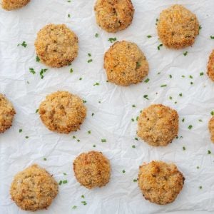 Golden brown tuna rice balls on crinkeled parchment paper scattered with chopped chives.