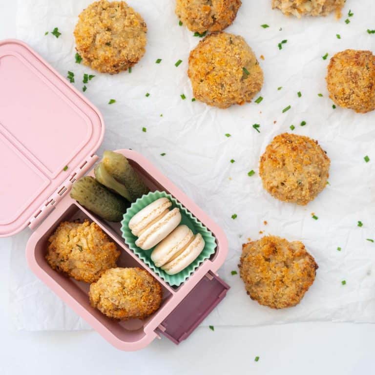 Tuna rice balls packed into a small pink bento box with cookies and vegetables.