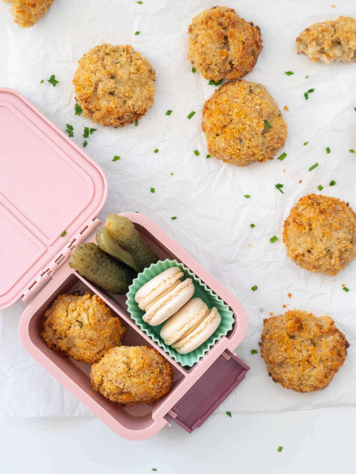 Tuna rice balls packed into a small pink bento box with cookies and vegetables.