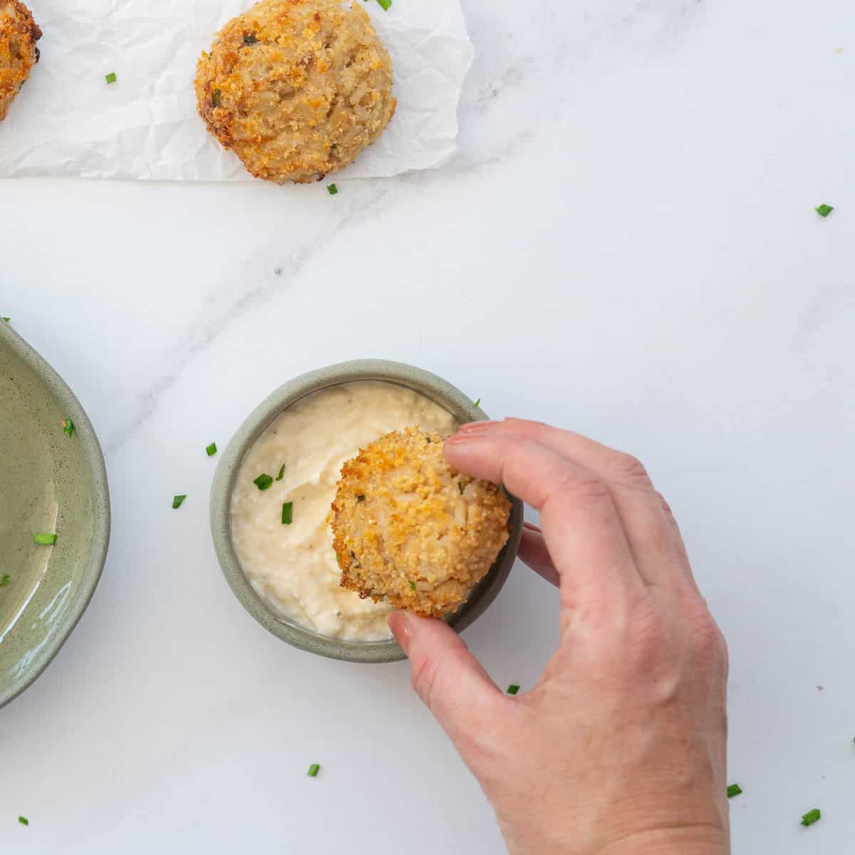 A tuna rice ball being dipped into a small bowl of aioli.