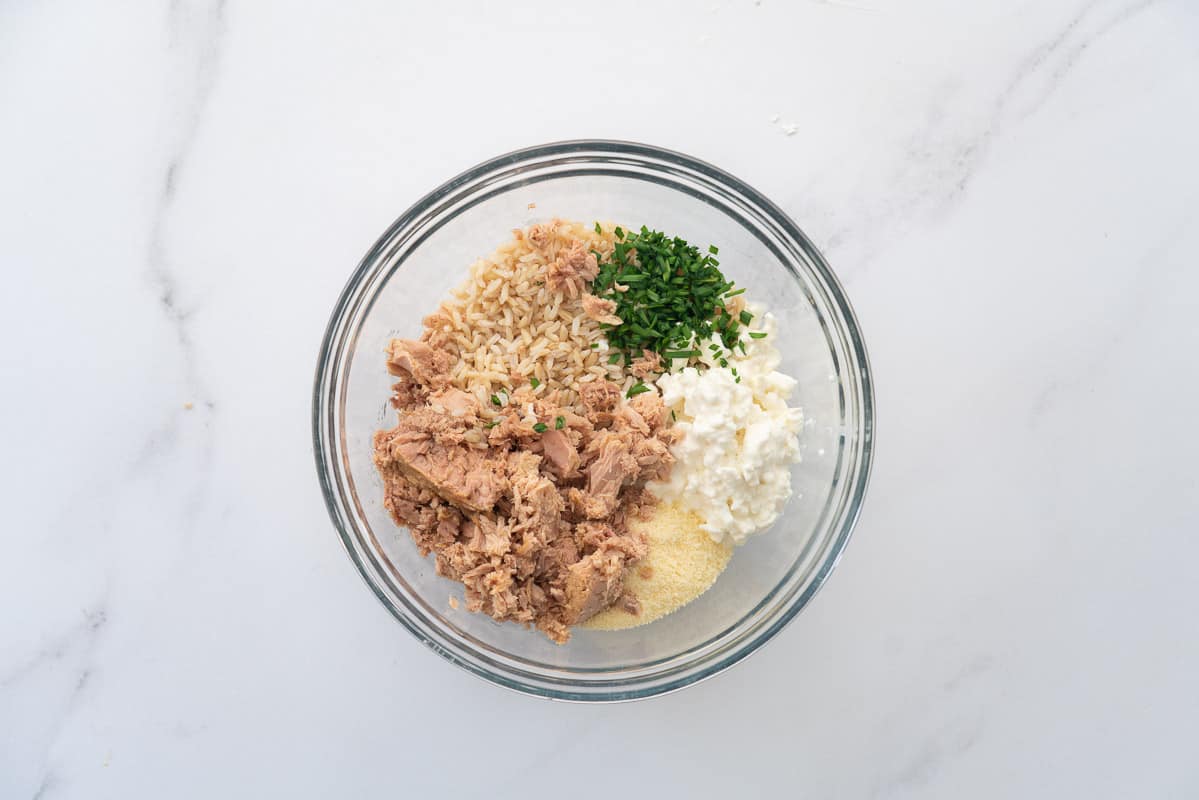 Brown rice, canned tuna, cottage cheese and chives in a glass mixing bowl. Ready to be mixed.