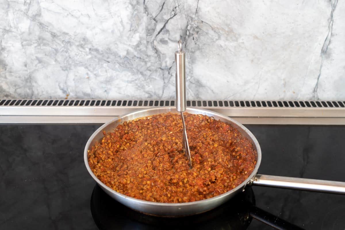 A potato masher mashing lentil based bolognese.