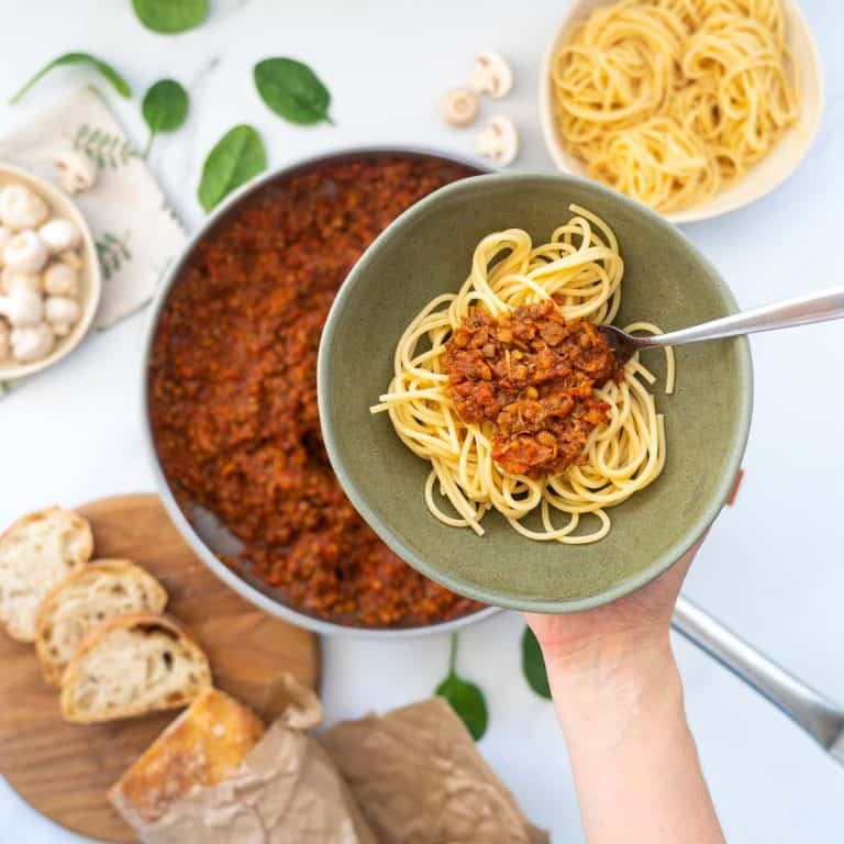 A bowl of vegan bolognese being held above a set dinner table.