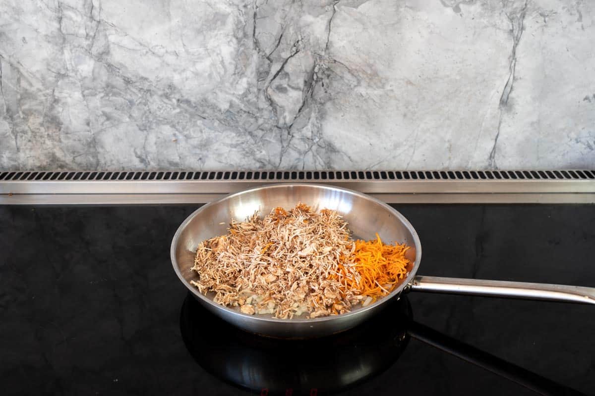 A large stainless steel fry pan with grated mushrooms and carrots.