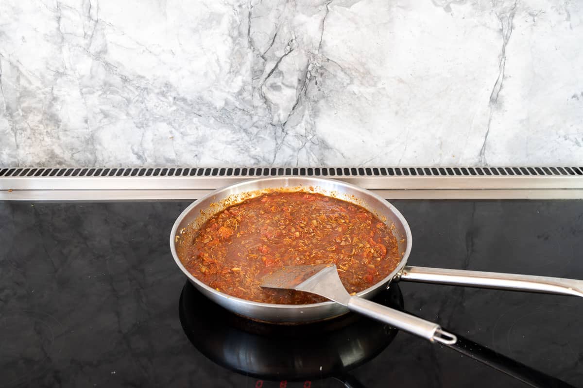 Tinned tomatoes, herbs and vegetables simmering on a stove top.